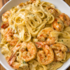 Creamy garlic shrimp Alfredo pasta made with tender fettuccine, juicy sautéed shrimp, and a rich Parmesan cream sauce, served in a white bowl for a comforting seafood dinner.