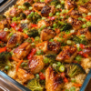 "Teriyaki chicken and rice casserole topped with roasted broccoli, red bell peppers, carrots, sesame seeds, and fresh green onions in a glass baking dish