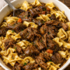 A comforting bowl of Crockpot Beef and Noodles made with tender slow-cooked chuck roast, soft egg noodles, and a rich, savory beef gravy, garnished with fresh parsley. This hearty slow cooker dinner is warm, flavorful, and perfect for cozy family meals, busy weeknights, or comforting Sunday suppers.