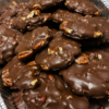 Homemade turtle candies with toasted pecans, soft caramel centers, glossy chocolate coating, and flaky sea salt, arranged on parchment for a holiday dessert tray.