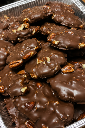 Homemade turtle candies with toasted pecans, soft caramel centers, glossy chocolate coating, and flaky sea salt, arranged on parchment for a holiday dessert tray.