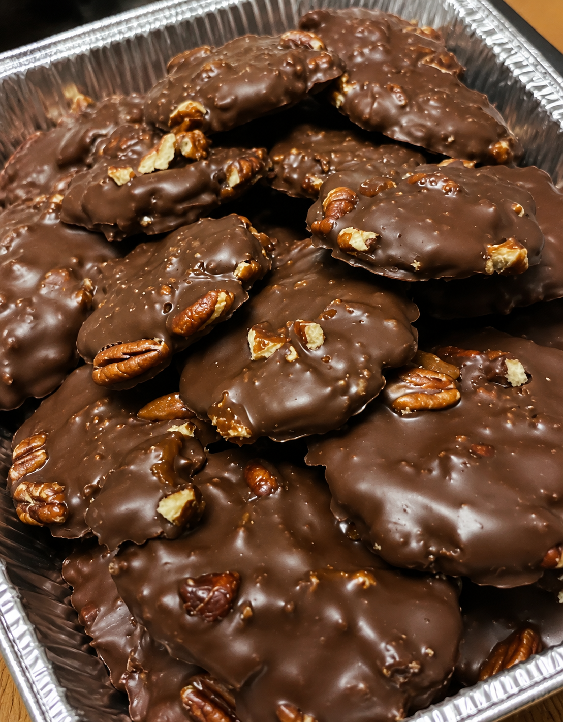 Homemade turtle candies with toasted pecans, soft caramel centers, glossy chocolate coating, and flaky sea salt, arranged on parchment for a holiday dessert tray.