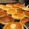 A tall stack of fluffy sourdough pancakes with crispy golden edges, topped with melting butter and drizzled with pure maple syrup. Served with fresh berries and a dusting of powdered sugar on a rustic plate, photographed in warm morning natural light with a cozy farmhouse breakfast setting.