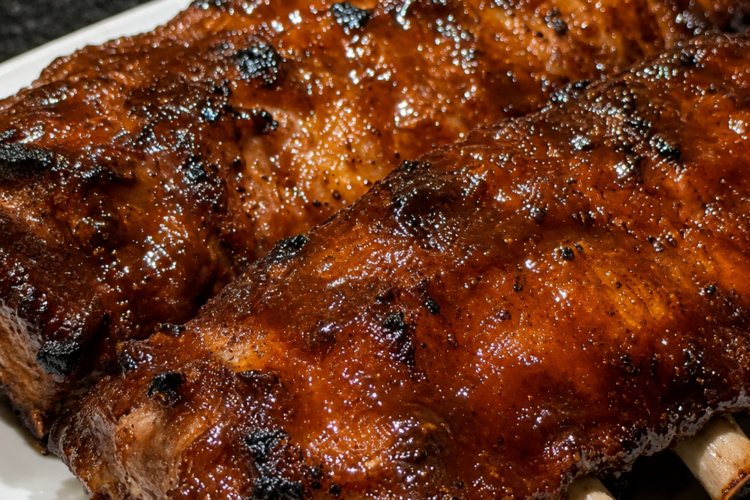 Tender Crockpot Barbecue Ribs coated in a glossy homemade barbecue sauce, slow-cooked until fall-off-the-bone and finished under the broiler for a sticky caramelized glaze. Served on a rustic wooden platter with extra barbecue sauce, fresh parsley, and classic sides like coleslaw and cornbread. Photographed in warm natural light, highlighting the juicy meat, rich smoky sauce, and irresistible barbecue finish.