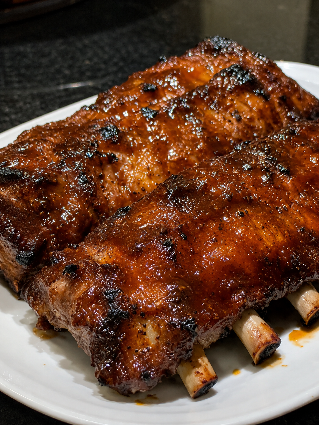 Tender Crockpot Barbecue Ribs coated in a glossy homemade barbecue sauce, slow-cooked until fall-off-the-bone and finished under the broiler for a sticky caramelized glaze. Served on a rustic wooden platter with extra barbecue sauce, fresh parsley, and classic sides like coleslaw and cornbread. Photographed in warm natural light, highlighting the juicy meat, rich smoky sauce, and irresistible barbecue finish.