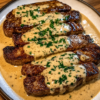Juicy pan-seared ribeye steaks sliced and topped with a rich, creamy garlic-Parmesan sauce. The steaks have a deep golden-brown crust and are served with silky sauce, fresh parsley, and roasted vegetables on a rustic plate. Photographed in warm natural light, highlighting the tender beef, creamy sauce, and restaurant-style presentation.