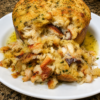 Golden-brown Cheddar Bay biscuits stuffed with a creamy lump crab filling and brushed with glossy lemon butter, arranged on a rustic serving platter. One biscuit is cut open to reveal tender chunks of crab, Parmesan, and buttery cracker filling inside the soft, fluffy cheddar-garlic biscuit. Garnished with fresh parsley and lemon wedges, with a small dish of melted lemon butter on the side in warm natural lighting.