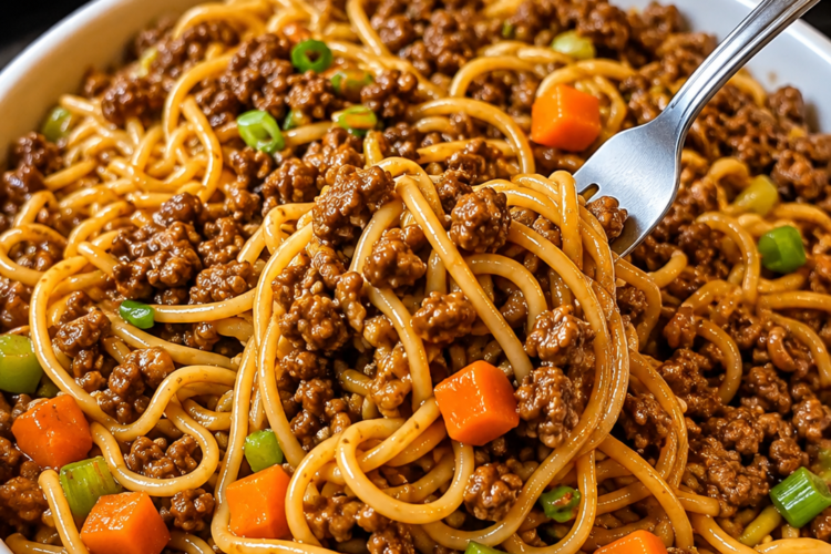 A close-up of homemade ground beef lo mein served in a rustic bowl, featuring tender spaghetti noodles coated in a glossy soy-garlic sauce with seasoned ground beef, crisp carrots, celery, and red onions. Garnished with sliced green onions and sesame seeds, the dish is photographed under warm natural light on a wooden table for a cozy, better-than-takeout presentation.