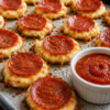 A close-up of crispy 2-ingredient pizza chips baked in a mini muffin pan, made with golden low-moisture mozzarella and mini pepperoni. The cheese forms lacy, crunchy edges while the pepperoni crisps on top. Served warm on a rustic wooden board with a small bowl of marinara dipping sauce and a sprinkle of Italian seasoning, photographed in warm natural light for an irresistible low-carb appetizer presentation.