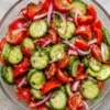 Fresh cucumber tomato salad with sliced cucumbers, juicy cherry tomatoes, red onions, fresh herbs, and a light vinaigrette dressing.