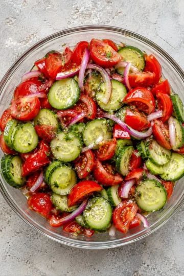 Fresh cucumber tomato salad with sliced cucumbers, juicy cherry tomatoes, red onions, fresh herbs, and a light vinaigrette dressing.