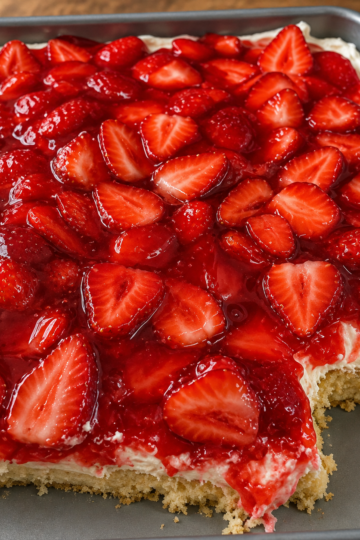 A slice of homemade strawberry graham cracker icebox cake showing soft, cake-like layers of graham crackers, fluffy vanilla whipped cream, and fresh sliced strawberries. The no-bake dessert is topped with extra strawberries and served chilled on a white dessert plate, photographed in warm natural light on a rustic wooden table for a fresh, summery homemade presentation.