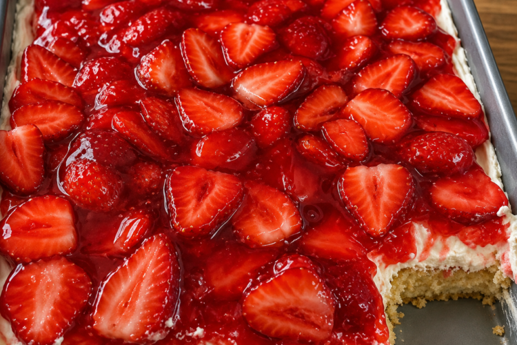 A slice of homemade strawberry graham cracker icebox cake showing soft, cake-like layers of graham crackers, fluffy vanilla whipped cream, and fresh sliced strawberries. The no-bake dessert is topped with extra strawberries and served chilled on a white dessert plate, photographed in warm natural light on a rustic wooden table for a fresh, summery homemade presentation.