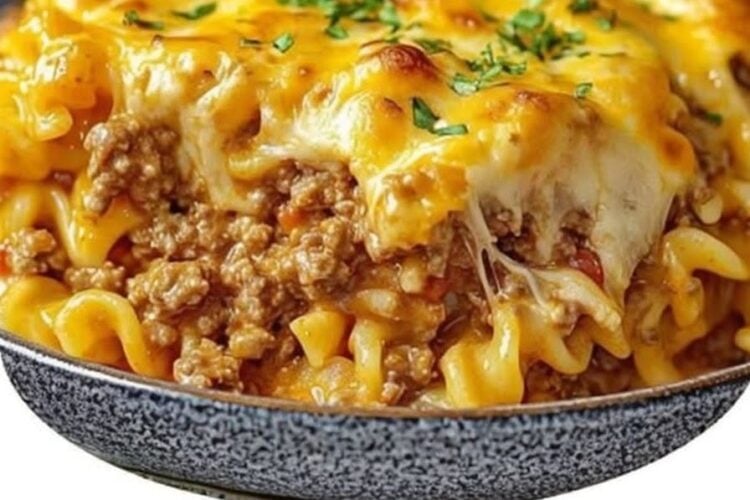 A hearty beef noodle casserole baked in a 9x13-inch dish with layers of tender egg noodles, seasoned ground beef in a rich tomato sauce, creamy cream cheese and sour cream filling, and a bubbling golden cheddar cheese topping. A serving is lifted onto a plate, revealing the creamy, cheesy layers, garnished with fresh parsley and photographed in warm natural light on a rustic w