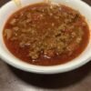 A bowl of hearty homemade ground beef and tomato soup with onions and diced vegetables in a rich red broth.
