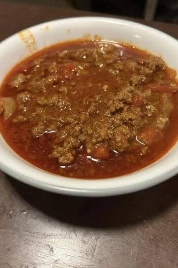A bowl of hearty homemade ground beef and tomato soup with onions and diced vegetables in a rich red broth.