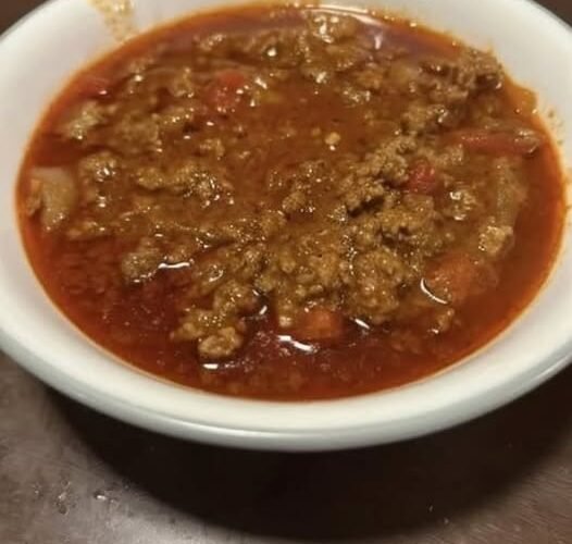 A bowl of hearty homemade ground beef and tomato soup with onions and diced vegetables in a rich red broth.