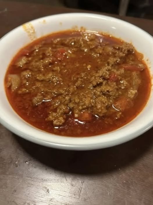 A bowl of hearty homemade ground beef and tomato soup with onions and diced vegetables in a rich red broth.