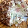 A creamy pineapple cheese ball coated in finely chopped pecans, served on a plate with buttery crackers and garnished with green onions.