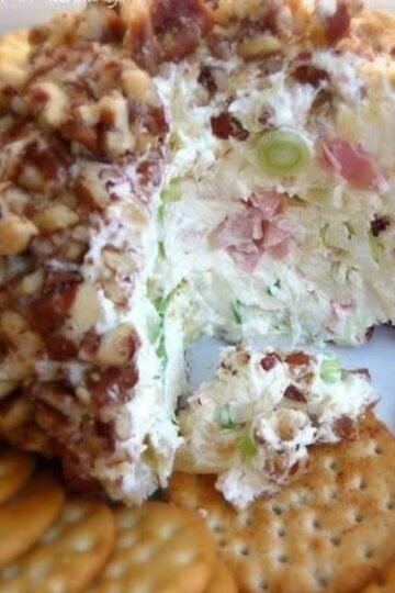 A creamy pineapple cheese ball coated in finely chopped pecans, served on a plate with buttery crackers and garnished with green onions.