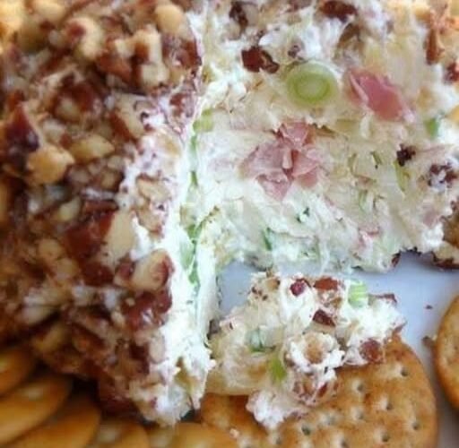 A creamy pineapple cheese ball coated in finely chopped pecans, served on a plate with buttery crackers and garnished with green onions.