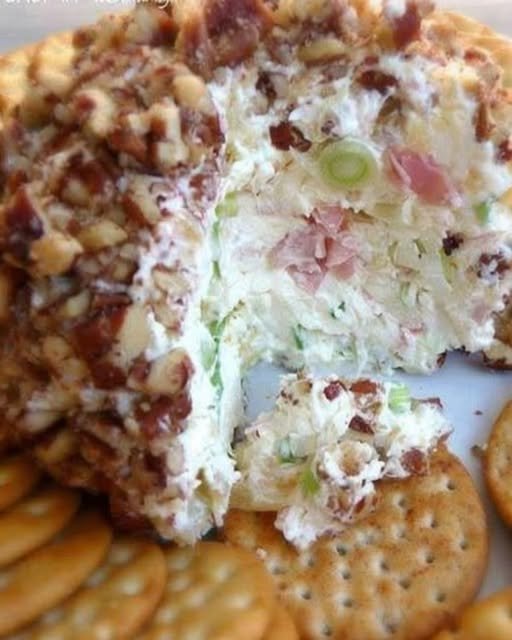 A creamy pineapple cheese ball coated in finely chopped pecans, served on a plate with buttery crackers and garnished with green onions.
