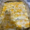 Creamy green chili chicken enchiladas baked in a foil pan, covered with melted Monterey Jack and cheddar cheese and a rich green enchilada sauce.