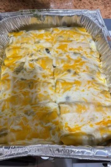 Creamy green chili chicken enchiladas baked in a foil pan, covered with melted Monterey Jack and cheddar cheese and a rich green enchilada sauce.