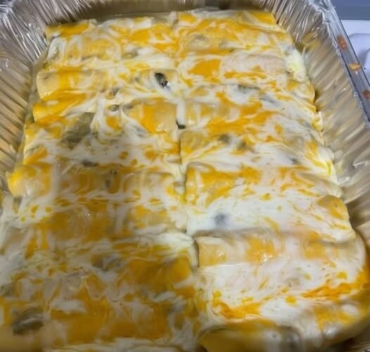 Creamy green chili chicken enchiladas baked in a foil pan, covered with melted Monterey Jack and cheddar cheese and a rich green enchilada sauce.