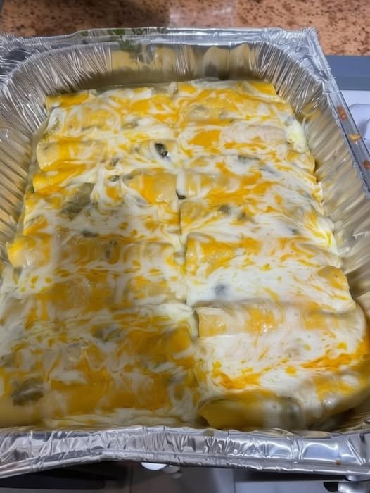 Creamy green chili chicken enchiladas baked in a foil pan, covered with melted Monterey Jack and cheddar cheese and a rich green enchilada sauce.