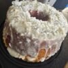 A moist coconut rum pound cake coated in creamy white glaze and generously covered with shredded coconut. The golden cake is served whole with a large slice missing, showing its rich, tender interior.