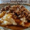 A comforting plate of creamy mashed potatoes topped with rich, savory ground beef gravy, featuring tender onions and a glossy peppery sauce, served hot in a bowl.