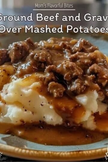A comforting plate of creamy mashed potatoes topped with rich, savory ground beef gravy, featuring tender onions and a glossy peppery sauce, served hot in a bowl.