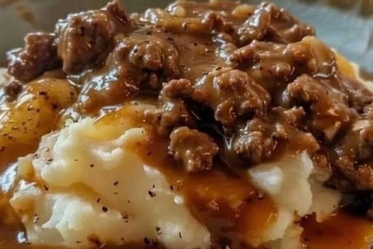 A comforting plate of creamy mashed potatoes topped with rich, savory ground beef gravy, featuring tender onions and a glossy peppery sauce, served hot in a bowl.
