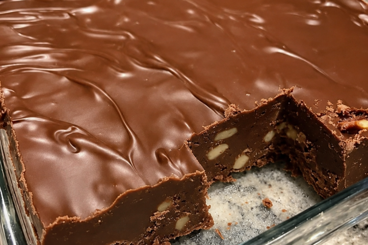 Close-up of rich old-fashioned chocolate fudge cut into neat squares and arranged on a rustic serving plate. The creamy homemade fudge is loaded with chopped nuts and has a smooth, glossy chocolate finish. Photographed in warm natural light with a few extra fudge pieces and chocolate chips scattered on a wooden table, creating a cozy holiday dessert presentation.