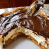 No-Bake Éclair Cake with layers of soft, cake-like graham crackers, creamy vanilla pudding filling, and a smooth rich chocolate frosting topping. The chilled dessert is sliced into neat squares, revealing the creamy layered center, and served as a nostalgic, chocolatey dessert perfect for potlucks and family gatherings.