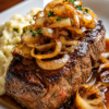 with a rich onion gravy made from deeply caramelized yellow onions, garlic, red wine, and beef broth. The fork-tender beef is arranged on a rustic platter, generously topped with glossy onion sauce and fresh thyme, alongside creamy mashed potatoes or traditional spaetzle. Photographed in warm natural light on a wooden farmhouse table for a cozy, comforting German-inspired dinner presentation.