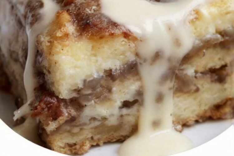 A warm cinnamon roll cake baked in a 9x13-inch pan, featuring a soft golden cake with swirls of buttery cinnamon and brown sugar throughout. A sweet vanilla glaze is drizzled over the top, melting into the warm cake and creating glossy, gooey pockets of cinnamon sweetness.