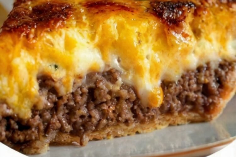 Homemade cheeseburger pie with a flaky golden crust filled with seasoned ground beef, sautéed onions and garlic, and melted cheddar cheese. The top is golden and bubbling with crisp, caramelized cheese around the edges, creating a hearty, comforting dinner.