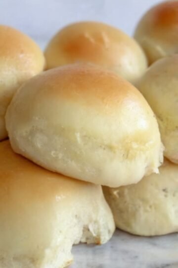 Soft, fluffy homemade dinner rolls baked until golden brown and glossy, with tender cloud-like centers. The warm rolls are brushed with melted butter and arranged together in a baking dish or basket, making a comforting side dish perfect for dinner, soup, or serving with butter and honey.