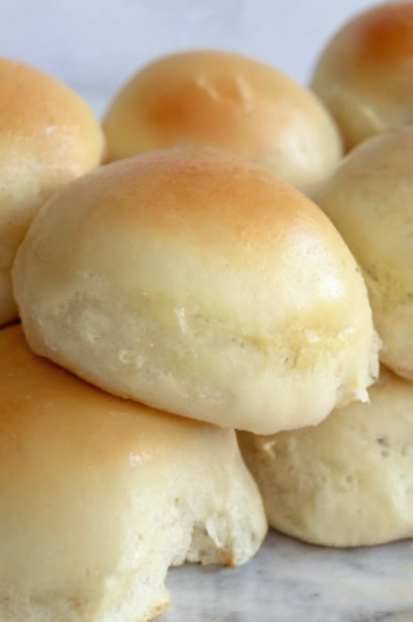 Soft, fluffy homemade dinner rolls baked until golden brown and glossy, with tender cloud-like centers. The warm rolls are brushed with melted butter and arranged together in a baking dish or basket, making a comforting side dish perfect for dinner, soup, or serving with butter and honey.