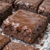 Fudgy chocolate brownies made with chocolate cake mix, topped with a thick, glossy chocolate frosting. The brownies have slightly crisp edges, a crackly top, and a rich, soft center, cut into neat squares and served as an indulgent homemade dessert.