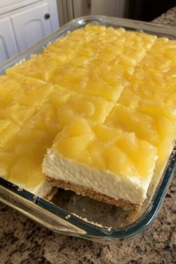 No-bake pineapple cream cheese dessert with a buttery graham cracker crust, a smooth and creamy sweetened cream cheese layer, and a glossy topping of crushed pineapple. The chilled dessert is cut into neat squares and served as a light, tropical, nostalgic treat.