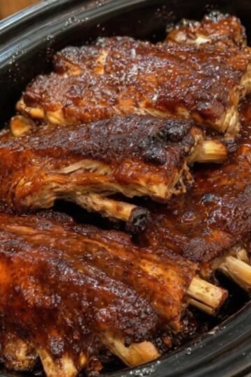 Slow cooker baby back ribs coated in a sweet, tangy barbecue sauce with brown sugar, apple cider vinegar, garlic, and smoked paprika. The ribs are fall-apart tender with a glossy, sticky caramelized glaze and slightly charred edges, served as a classic comfort-food barbecue dinner.