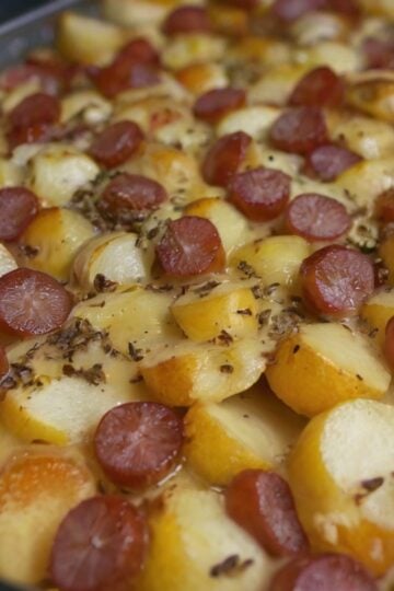 A hearty Smoked Sausage and Potato Bake featuring sliced smoked sausage, tender golden Yukon gold potatoes, and diced green and yellow bell peppers roasted together with butter, olive oil, oregano, and basil. The sausage and potatoes have lightly caramelized edges and are served hot in a rustic baking dish for a cozy, one-pan family dinne