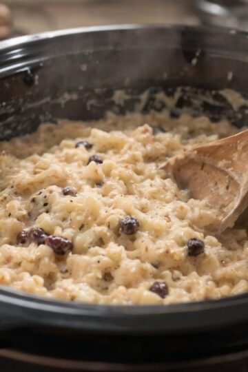 Creamy slow cooker rice pudding made with tender short-grain rice, whole milk, cinnamon, vanilla, and plump raisins. Served warm in a bowl with a light sprinkle of cinnamon on top, showcasing its thick, custardy texture and classic old-fashioned comfort.