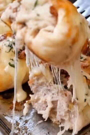Golden-brown stuffed breadstick bombs filled with creamy chicken Alfredo, crispy bacon, melted mozzarella, and Parmesan cheese. The soft baked dough has a buttery garlic-Parmesan topping, with the cheesy filling visible inside. Served warm on a parchment-lined baking sheet as an irresistible appetizer or comfort-food snack.