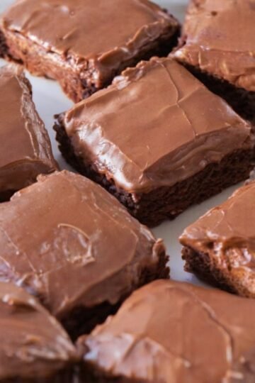 A tray of thick, fudgy chocolate brownies topped with a smooth, glossy chocolate icing that has set into a delicate crackly finish, cut into neat squares and ready to serve.