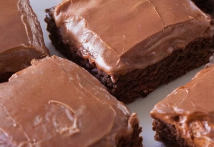 A tray of thick, fudgy chocolate brownies topped with a smooth, glossy chocolate icing that has set into a delicate crackly finish, cut into neat squares and ready to serve.