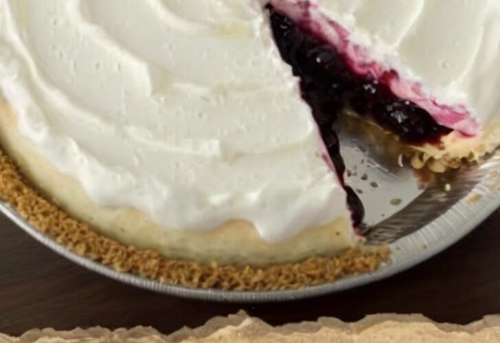No-bake blueberry cream pie with a graham cracker crust, creamy white cheesecake filling, and glossy blueberry topping swirled across the surface, with one slice removed.